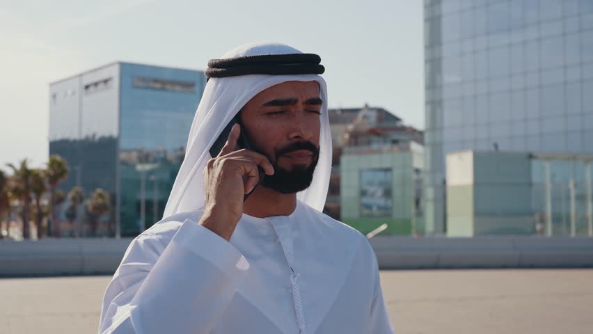 Handsome man with united arab emirates traditional kandura spending time outdoor in the city. Emirati young businessman from Dubai on a phone call.