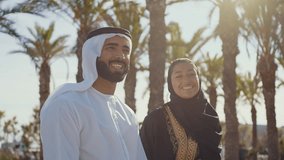 Cinematic image of a young couple from the united arab emirates spending time outdoor. Man and woman with traditional emirati kandura and abaya conversating while sitting on a bench at the park. - Powered by Shutterstock - Get 15% off with code: PIKWIZARD15