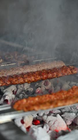 Cooking shish kebab and meat skewers, on a grill, Turkish Adana kebab on fire with smoke, turkish food adana kebab grilled. Meat and vegetables on grill. Traditional Turkish kebab grilled on skewers
