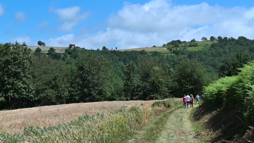 Sale san Giovanni,Piemonte,Italy. Escape from city life among the green hills and countryside: a group of people are walking along the path taking a pleasant stroll. Beautiful summer day.