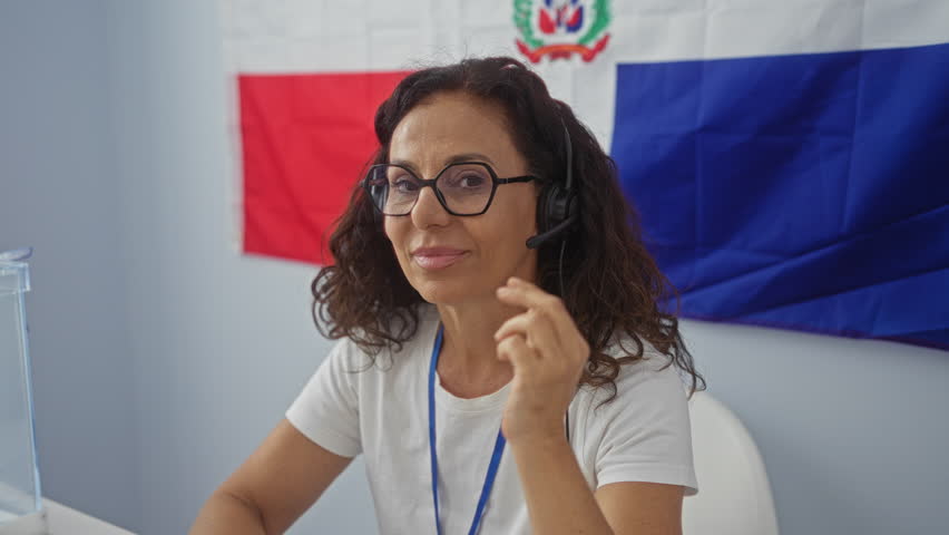 Woman smiling at electoral college in the dominican republic indoors with a headset and flag in the background