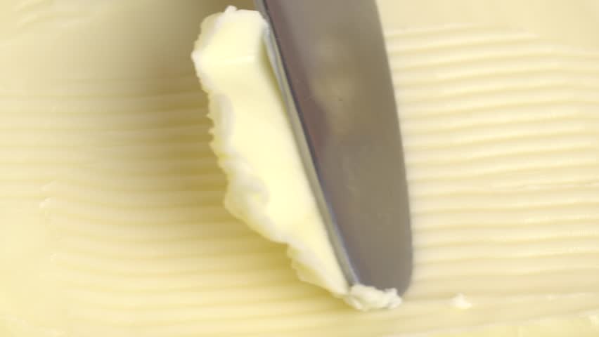 Knife scoops butter, close up.