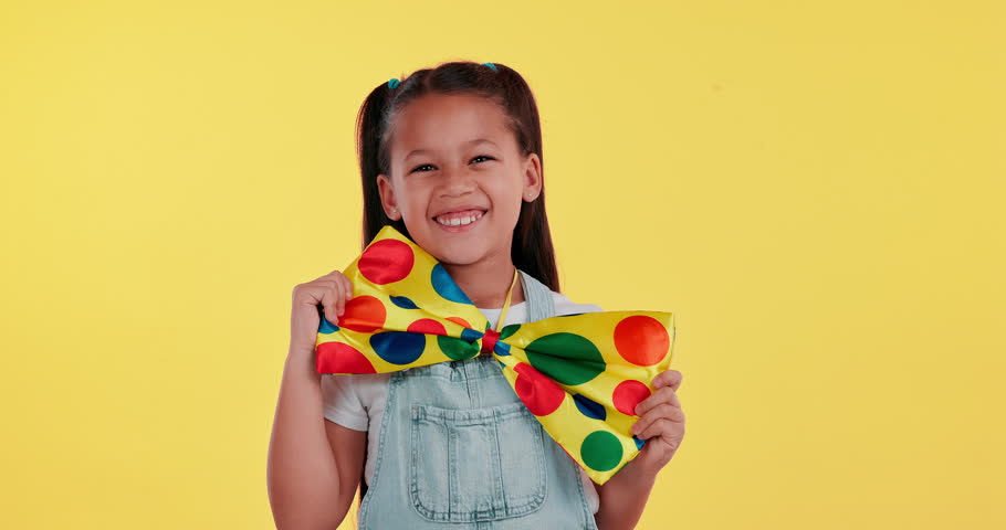 Young girl, happy and bow tie on studio background for playful, innocent and fashion with face. Child, portrait and smile in dungaree with polkadot color necktie with excitement for back to school