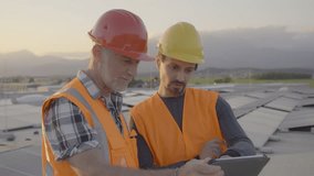 Electricity engineers checking solar panels array connection on digital tablet, medium shot. Two caucasian electricians maintaining PV modules system on building rooftop during sunrise - Powered by Shutterstock - Get 15% off with code: PIKWIZARD15