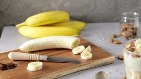 Two bowls of overnight oats topped with banana slices and almonds. A spoon, cutting board, knife, and a blue napkin rest nearby. - Powered by Shutterstock - Get 15% off with code: PIKWIZARD15