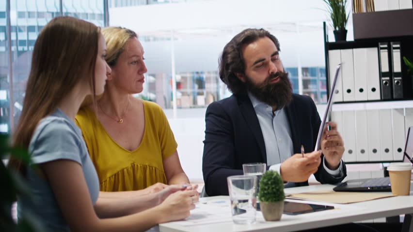 Financial advisor talks with clients about importance of budgeting in income management, offering them written guide. Mom and daughter explore best practices for building money saving habits, camera A