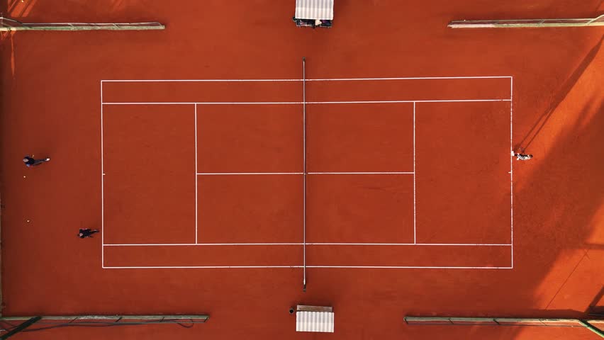 Three men practice tennis serves on clay court. Top steady aerial camera