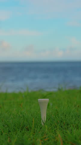 Golfer placing golf ball on the tee at golf course. Close up. Male hand in a golf glove puts the ball on the field on the background of the blue ocean