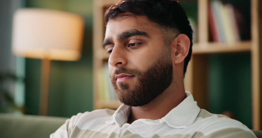 Man, thinking and sad in lounge with anxiety from bad memory, conflict or news in home. Indian guy, stress or thoughts in living room with depression, regret and mental health or lonely in apartment