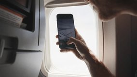 Young man enjoying the view from plane seat takes a photo using his cellphone. Looking outside airplane window male hold smartphone to window glass and takes a picture of the aircraft's wing and view - Powered by Shutterstock - Get 15% off with code: PIKWIZARD15