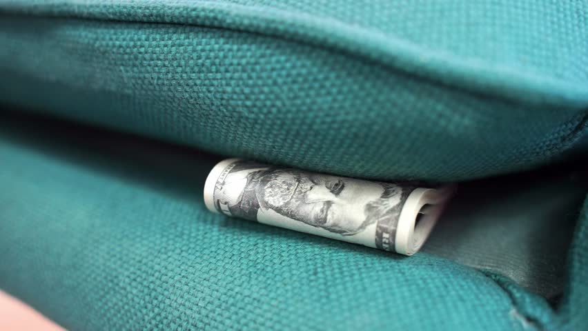 Dog paw pulls out money, rolled banknotes from under the sofa cushions close-up Cash dollars hidden for rainy day, financial airbag, savings, investments Distrust of banks, keep savings at home, risk