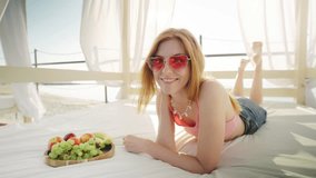 A woman is peacefully enjoying a beautiful day on a beach bed, relishing fresh fruit in a serene seaside paradise under warm sunlight, looking carefree and joyful in this paradise - Powered by Shutterstock - Get 15% off with code: PIKWIZARD15