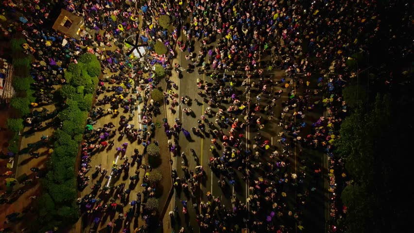 Aerial night shot of a large-scale protest in Tbilisi, Georgia, with crowds holding flags and phone lights