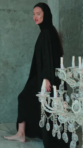 Young beautiful woman in black arab national dress abaya walking barefoot around a large chandelier