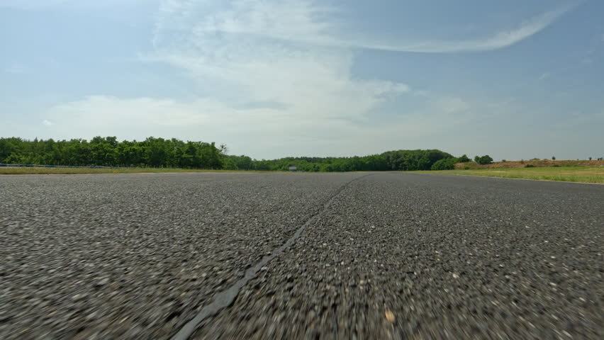 POV: High speed action shot of driving around the empty winding race track during a fun track day. Driving down the empty race circuit in the scenic countryside on a sunny summer day. Motorsport hobby