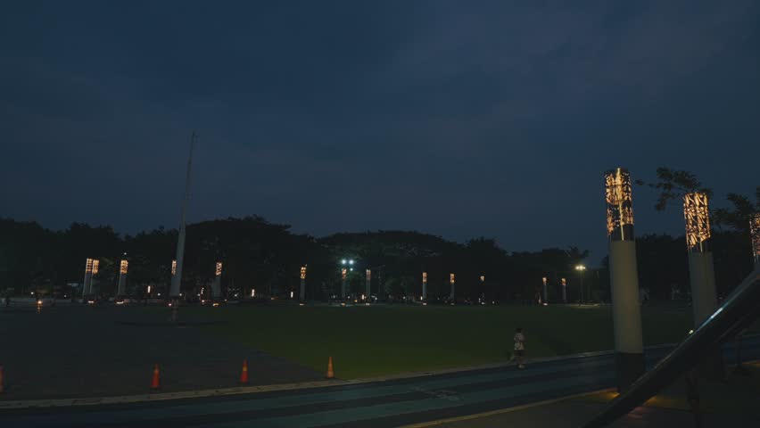 A dimly lit park at night with illuminated light posts and a dark sky.