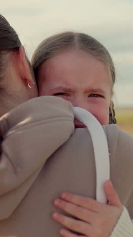 Loving young mother hugs and soothes her little daughter. Child is crying in park in arms of mom. Mommy soothes baby. Family mother and child with tears in their eyes hugs their mother, emotionally