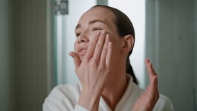 Beauty girl massaging serum on face closeup. Attractive woman applying moisturizing cream in daily routine at home. Serene young lady looking camera rubbing rejuvenating cosmetics in skin in bathroom. - Powered by Shutterstock - Get 15% off with code: PIKWIZARD15