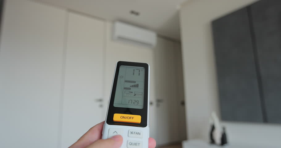 Man adjust the temperature on air conditioner in the living room. Hand uses air conditioner remote control.