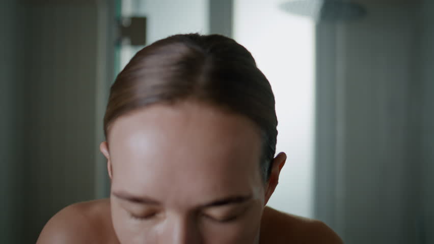 Morning girl washing face at home closeup. Serene young woman splashing water looking camera. Beautiful lady cleansing ideal smooth skin enjoying skincare routine. Refreshing wellness routine concept.