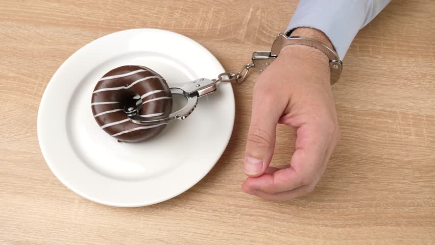 A handcuffed man pushes away a chocolate donut. Passion for sweets.
