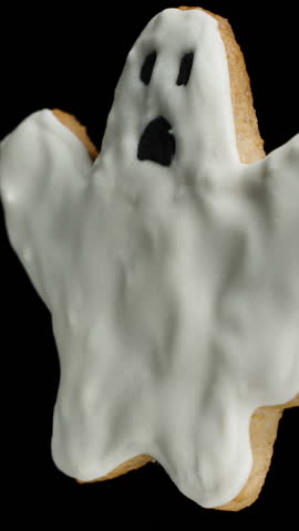 Vertical video. A Ghost-Shaped Cookie Painted with White Sugar Icing, Looping Rotation. Isolated on Black, Holiday Theme.