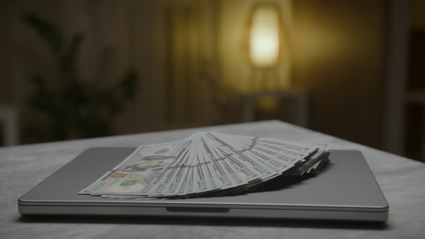 Fan of hundred dollar bills placed on a closed laptop