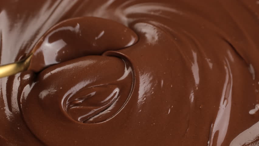 Stirring melted dark chocolate with golden spoon, close up. Liquid chocolate swirl