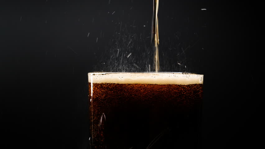 Pouring cola into a glass. Cola with ice and bubbles in glass. Soda close-up. Food background. Turning a glass of cola. Macro photography. Close-up.