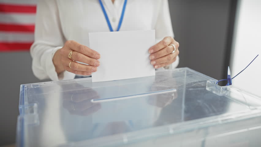 Adult woman voting indoors at a us electoral center with flag in background