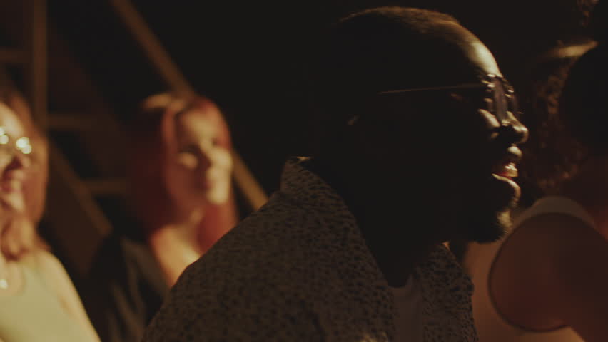 Young diverse people sitting in audience and laughing at jokes during stand-up show. Rack focus shot