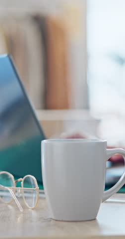 Coffee, glasses and steam with a cup on an office desk while a business person is working in the background. Tea, cup or mug with an employee typing on a laptop in a workplace for communication