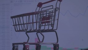 Modern economics. Business concept of securities trading. A small shopping cart from a supermarket stands against the background of a computer monitor on which economic data is changing. Close-up. - Powered by Shutterstock - Get 15% off with code: PIKWIZARD15