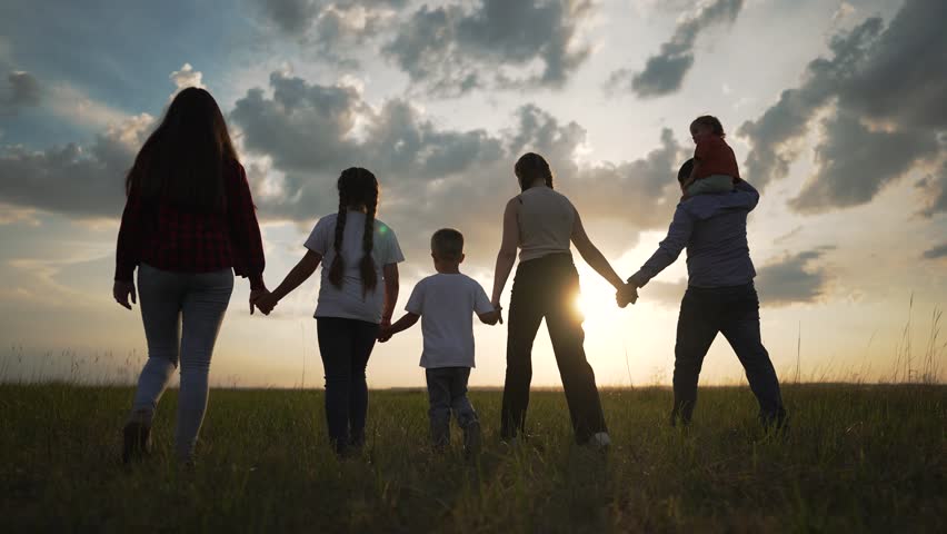 Happy group people walking outdoors at sunset. Family unity friendship in nature. Silhouette happy group enjoying scenic walk. People bonding and holding hands. Togetherness and joy in group setting.