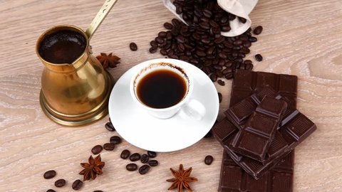sweet hot drink : black coffee with beans in a white bag on a wooden table with stripes of dark chocolate and copper cezve