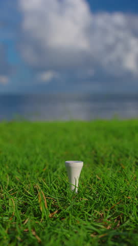 Golfer placing golf ball on the tee at golf course. Close up. Male hand in a golf glove puts the ball on the field on the background of the blue ocean