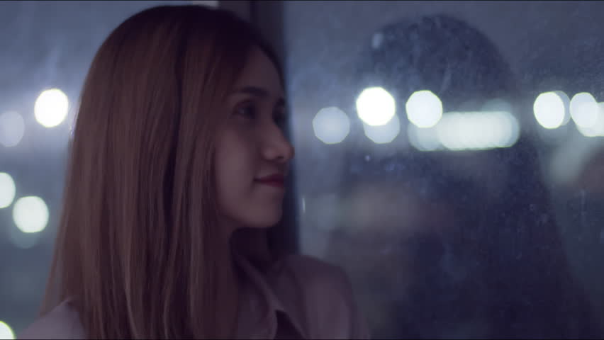 A young woman stands and looks out of the bedroom window.