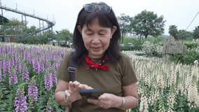 Asian woman crouching to take photo of purple foxglove flowers in garden using smartphone camera, capturing detailed shots amidst diverse array of blooming, lifestyle middle-aged woman traveling alone - Powered by Shutterstock - Get 15% off with code: PIKWIZARD15
