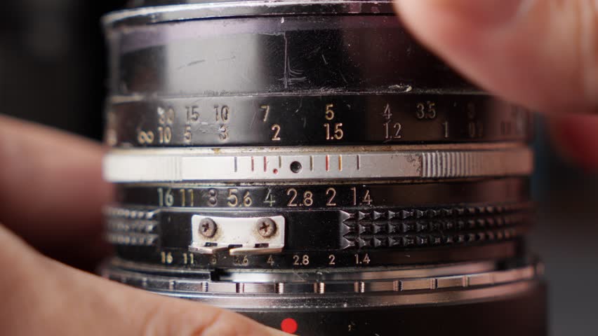 Close up shot of hands turns vintage camera lens focus ring, numbers to infinity