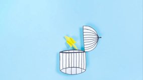 Concept of gaining freedom, removing limiting attitudes, beliefs, liberation from the cage. Yellow bird flies out of the opening cage. Blue background. Flat lay. Stop motion animation. - Powered by Shutterstock - Get 15% off with code: PIKWIZARD15