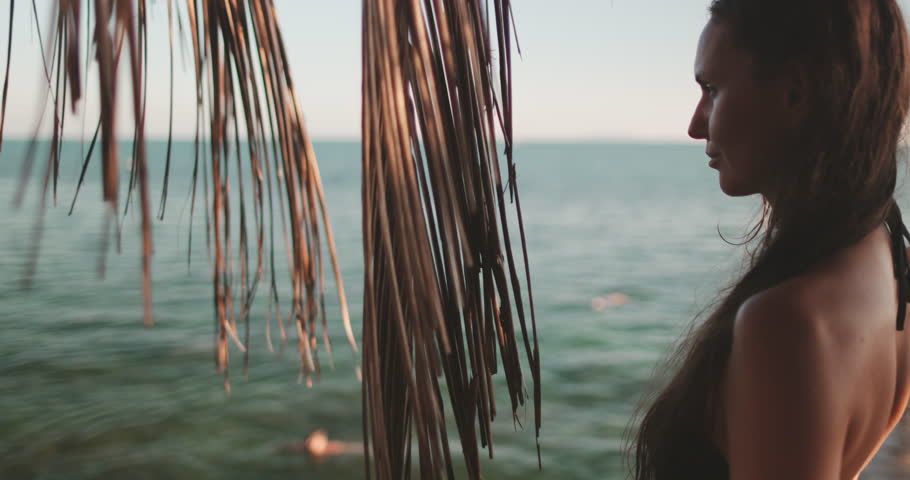 Close up portrait girl on summer holiday vacation on tropical sea island. Woman stands next to a palm tree on the sandy beach beside the ocean in Thailand, with waves gently crashing in the background