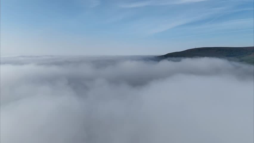An aerial timelapse above the fog revealing mountain and blue sunny sky with clouds