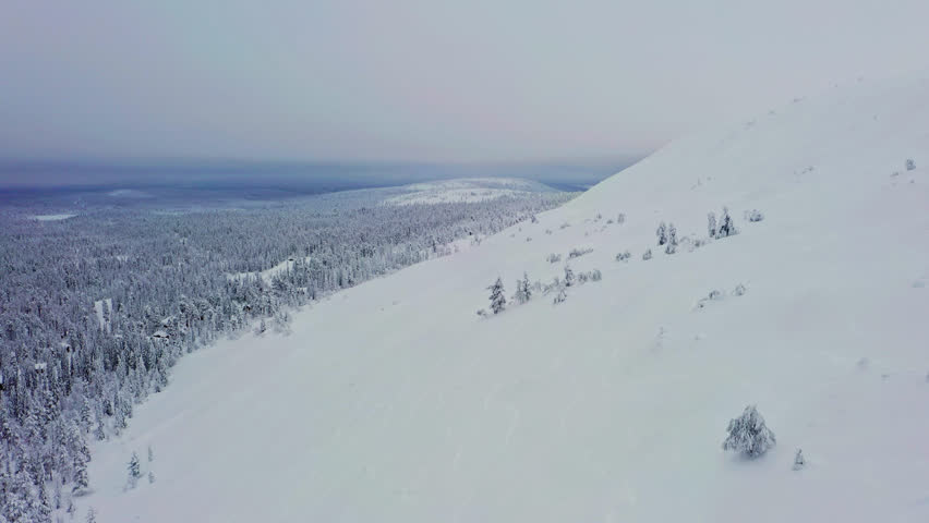 Drone flying along the snowy Luosto fell, gloomy winter day, in Lapland, Finland
