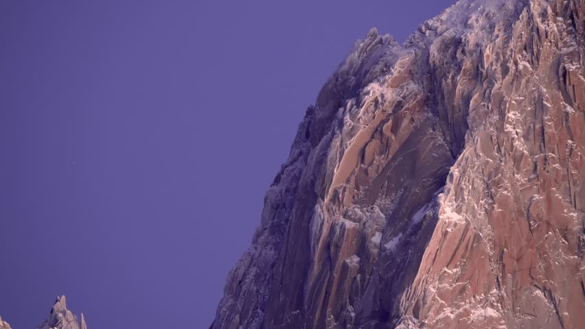 Backward zoom-out static view reveals Mount Fitz Roy under the morning purple sky with its rocky steep peaks in Patagonia, Argentina