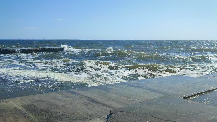 Storm. Storm at sea. Large high sea waves with white foam hitting concrete pier wall and splashing on hot sunny summer day. Stormy sea weather. Rough sea. Shore and waves. Nature. Natural background