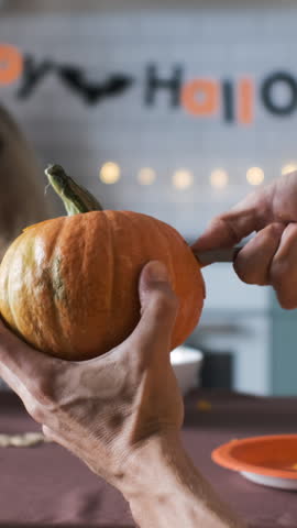 Vertical video. Close-up of father making Jack-o-Lantern while his daughter painting scary face on pumpkin at home, selective focus