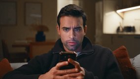 Frustrated man reading message smartphone in dark home living room closeup. Dissatisfied guy reacting nervously on cellphone sms at home couch. Worried businessman looking mobile phone screen on sofa. - Powered by Shutterstock - Get 15% off with code: PIKWIZARD15