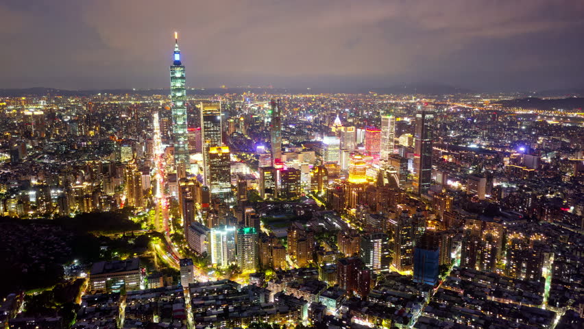 Aerial hyperlapse at night above Downtown Taipei, the vibrant capital of Taiwan, with 101 Tower standing out among skyscrapers in Xinyi Commercial District and city lights dazzling in the dark