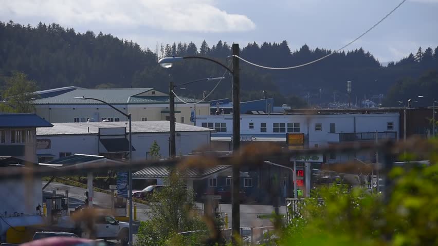 A shot of cars passing on the road and with some houses in Kodiak Alaska.