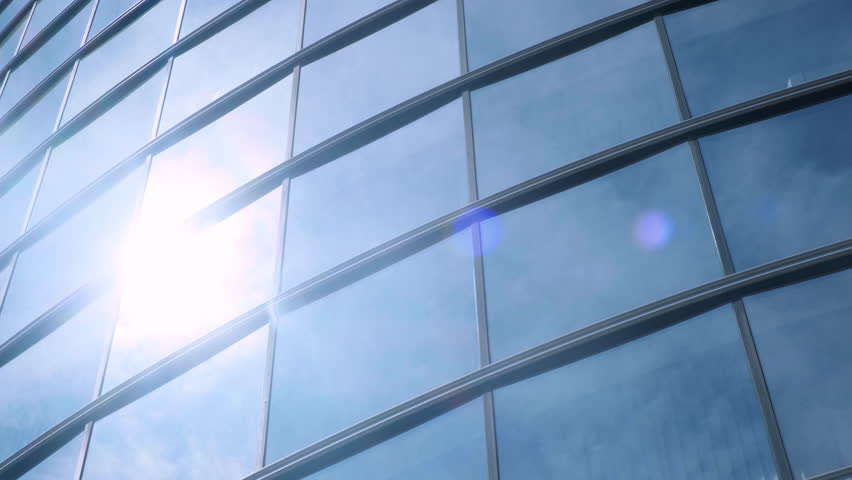 Modern walls are made of glass and steel with reflections of buildings, sunlight and sky.